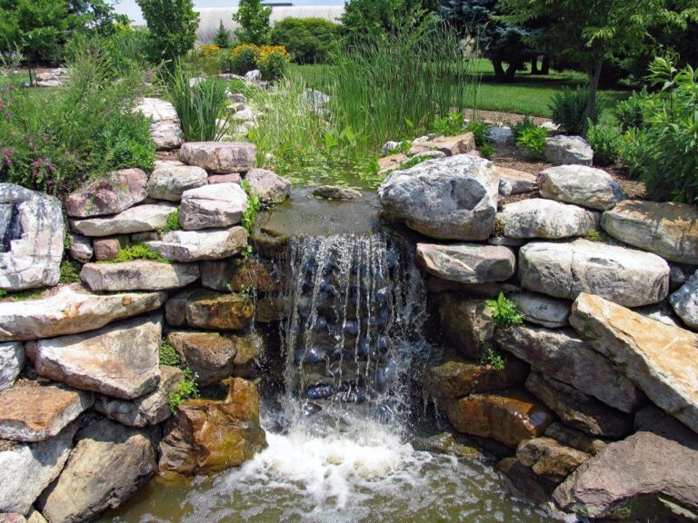 New backyard waterfall installation flowing over stone beside landscaped patio seating