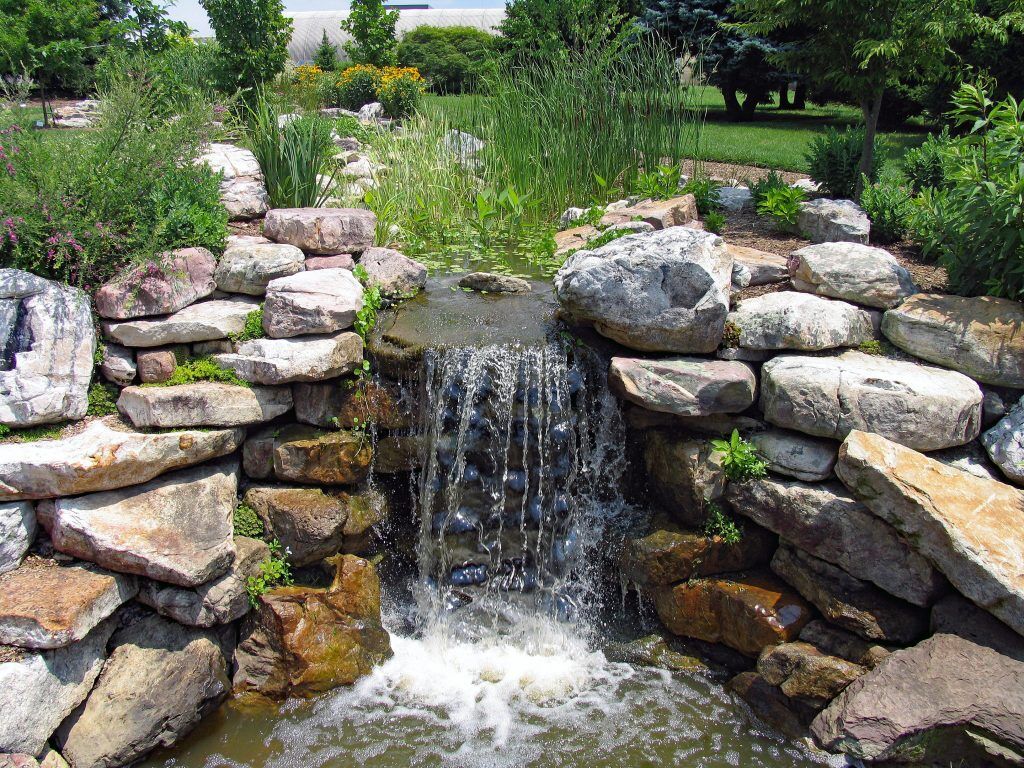 New backyard waterfall installation flowing over stone beside landscaped patio seating