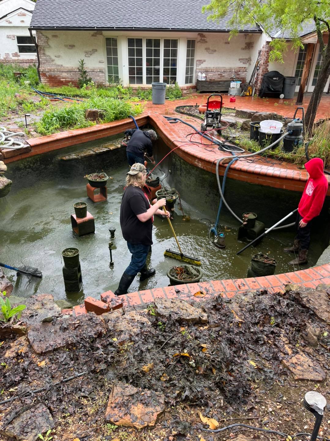 Specialist performing Pond Maintenance in a landscaped El Reno, OK backyard while inspecting water flow and pond edges