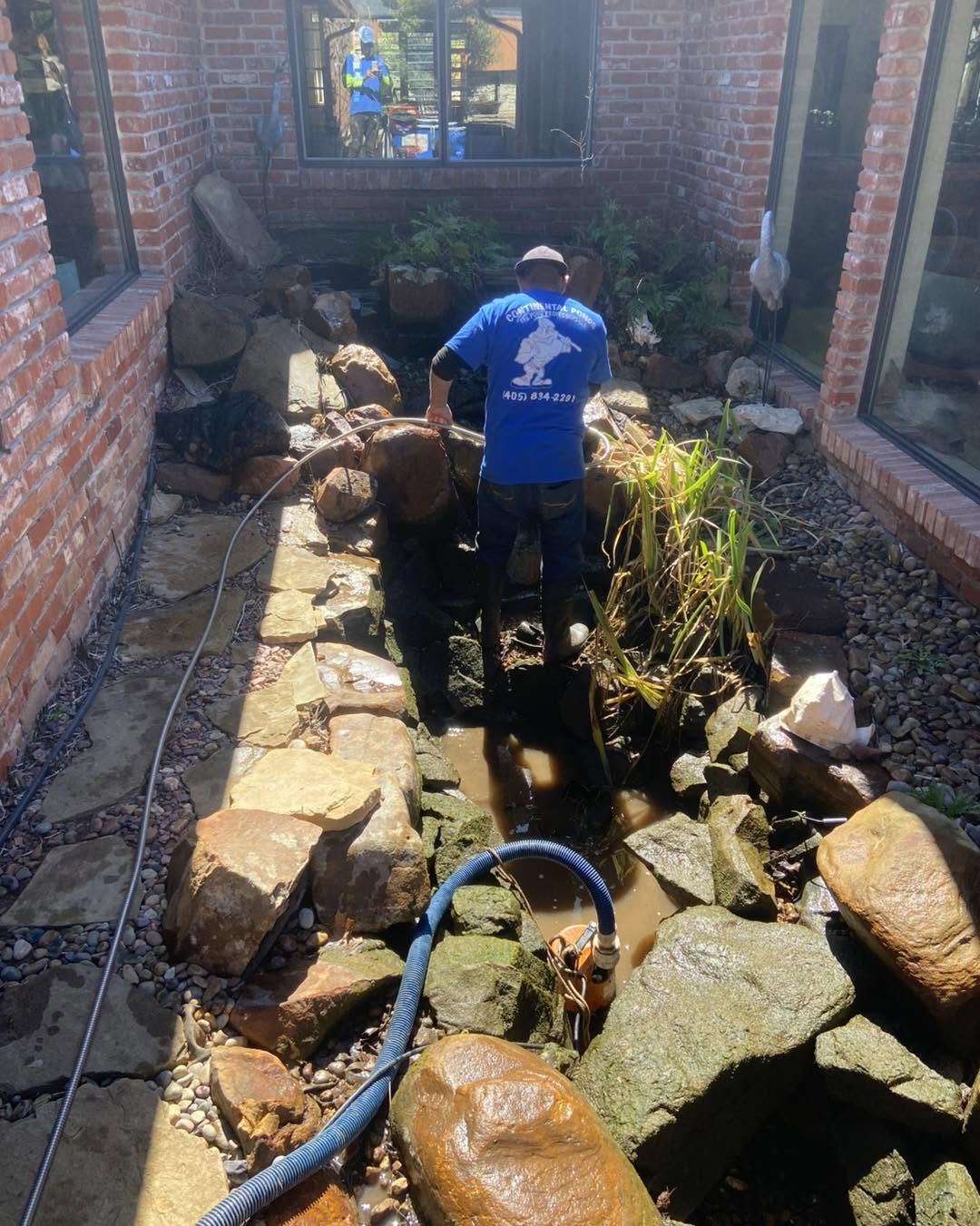 Pond specialist cleaning rocks and removing sludge during Oklahoma City pond cleanout