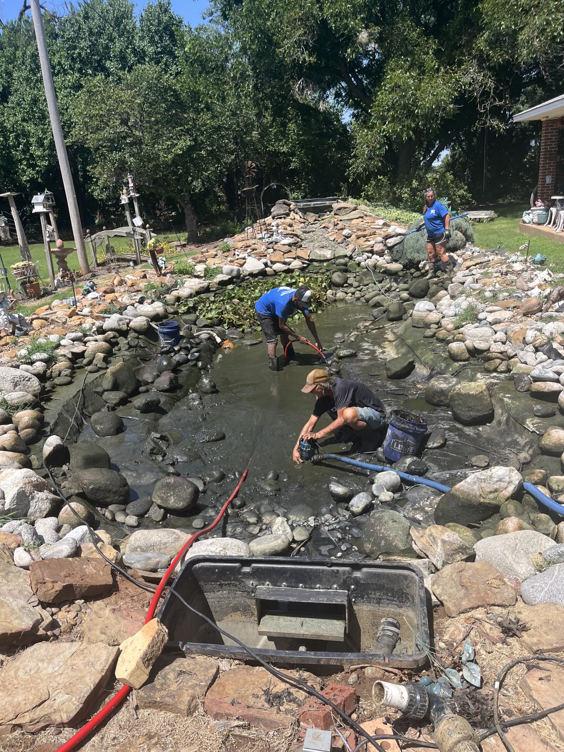 Pond Maintenance in Edmond, OK in progress as a technician cleans a skimmer beside a garden pond