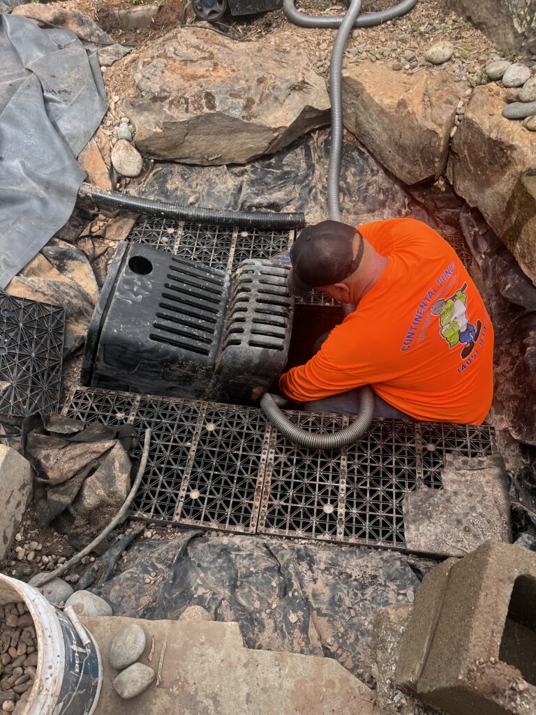 Continental Ponds technician cleaning a pondless waterfall basin in Edmond, Oklahoma