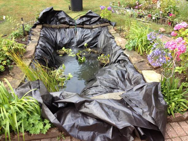 Technician performing pond maintenance beside a Moore, OK backyard water feature while checking pump flow