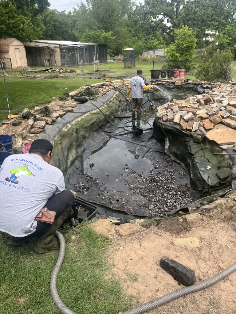 Continental Ponds technician cleaning a drained pond with hoses in Jones, Oklahoma